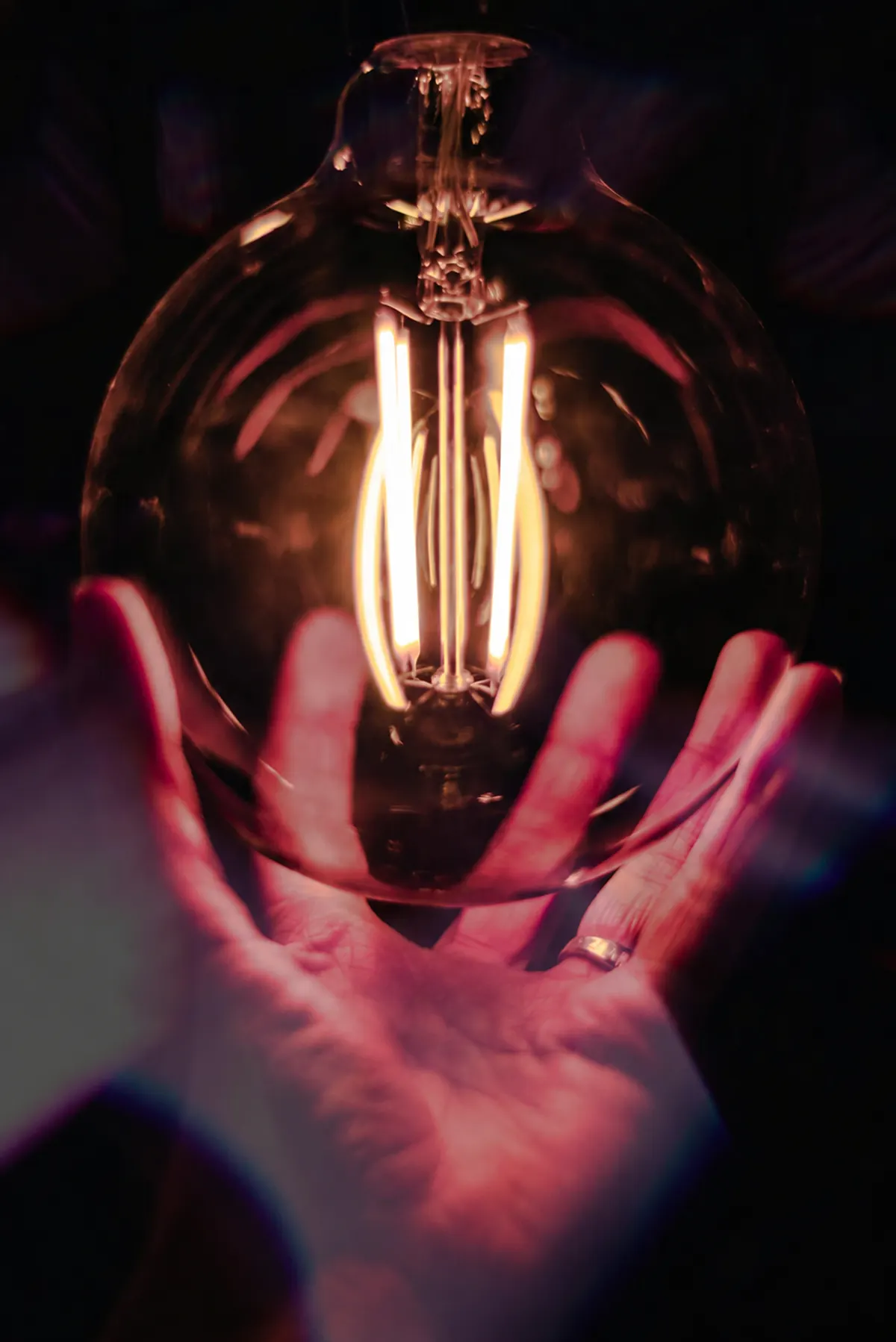Hand holding a glowing filament light bulb in a dark room